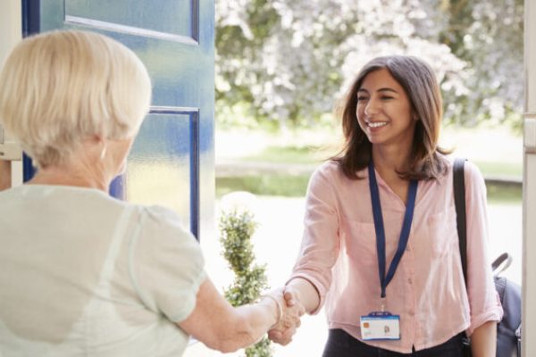 Senior woman greeting female care worker making home visit